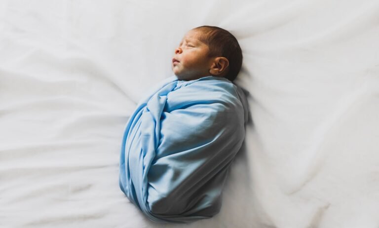 Swaddled newborn sleeping peacefully in a blue wrap