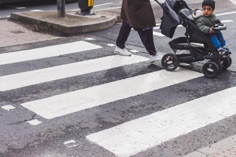 Parent pushing a baby stroller across a city crosswalk