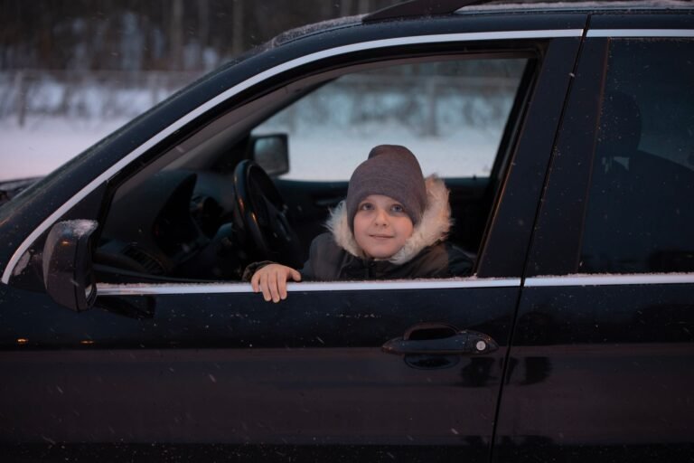 A young child in winter clothing riding in a car on a snowy day