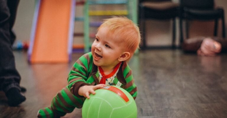 Smiling baby crawling with a green ball in an indoor play space