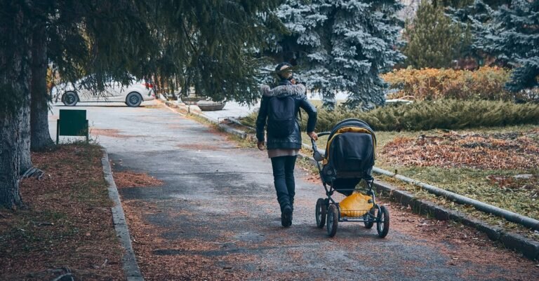 Parent walking with a stroller along a park path on a cool autumn day